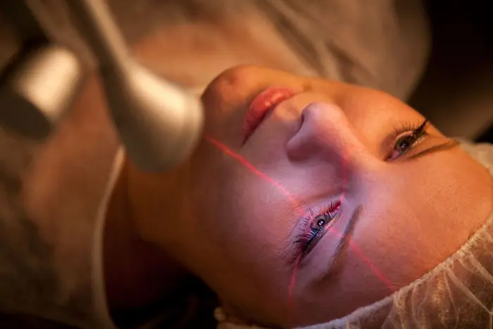 Frau liegt auf einem OP Tisch mit einem roten Laserkreuz über das Gesicht.